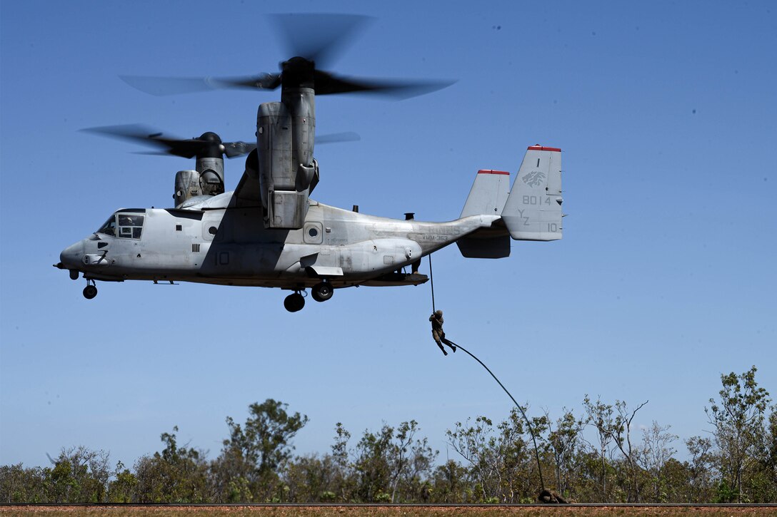 A Marine slides down a rope out of an aircraft.