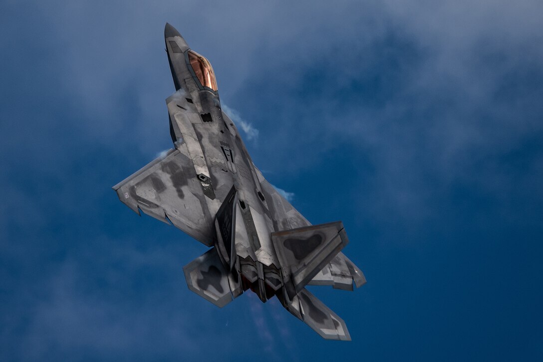 A military fighter jet flies against a blue sky.