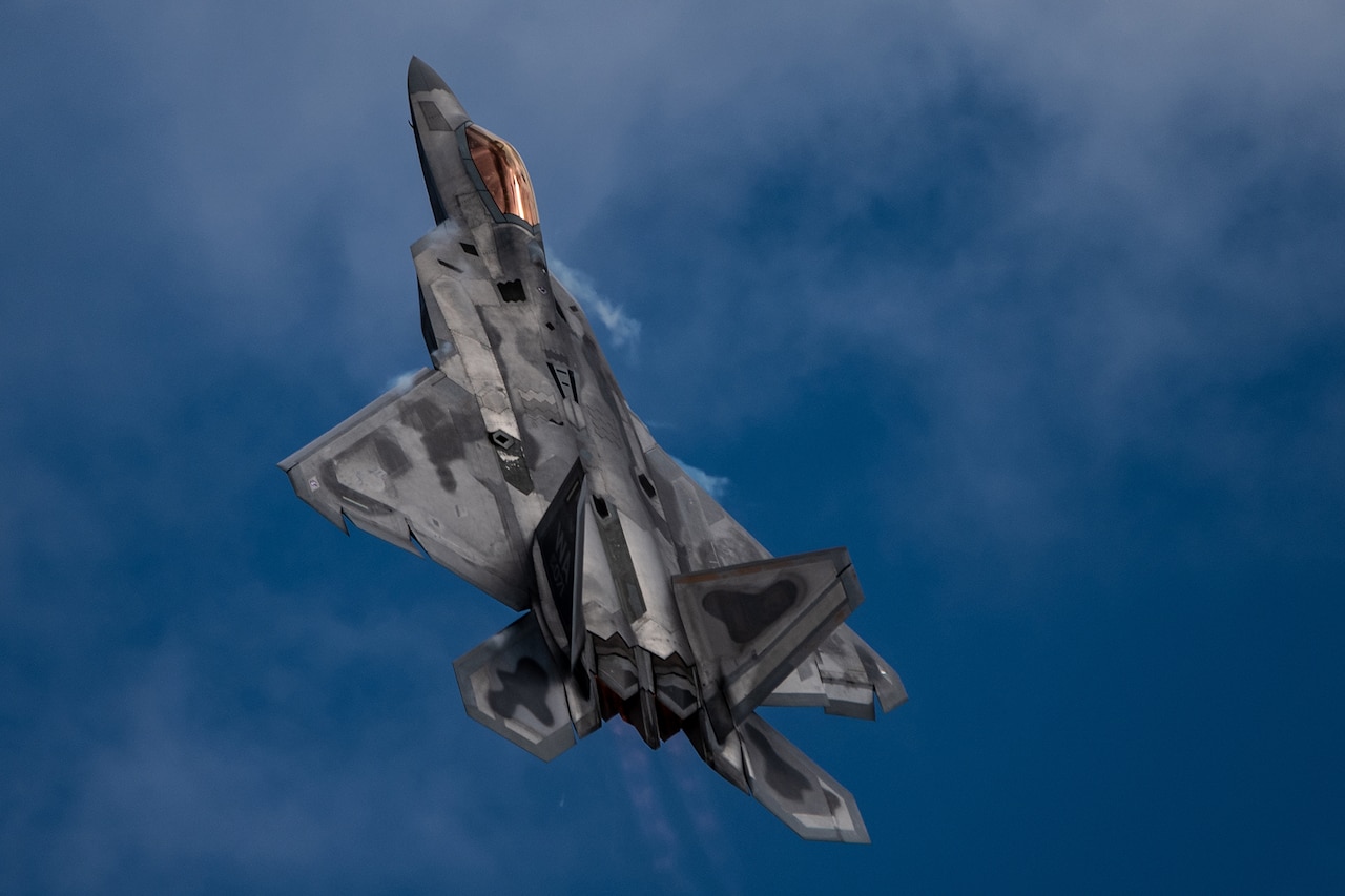 A military fighter jet flies against a blue sky.