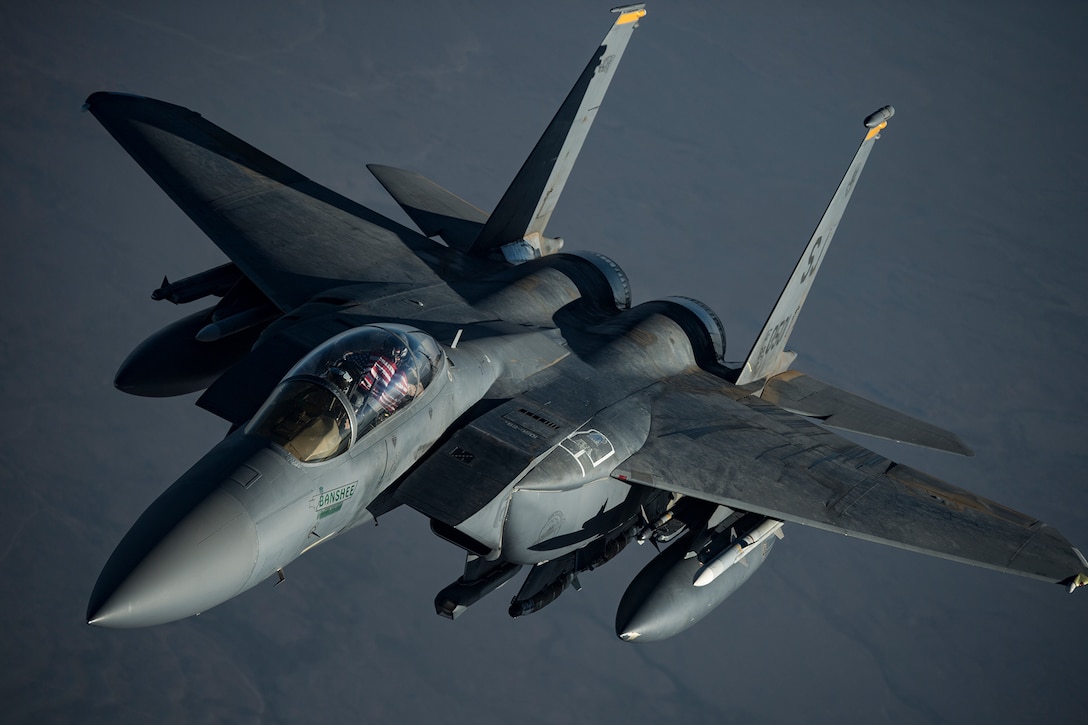 A military fighter jet flies against a gray background.