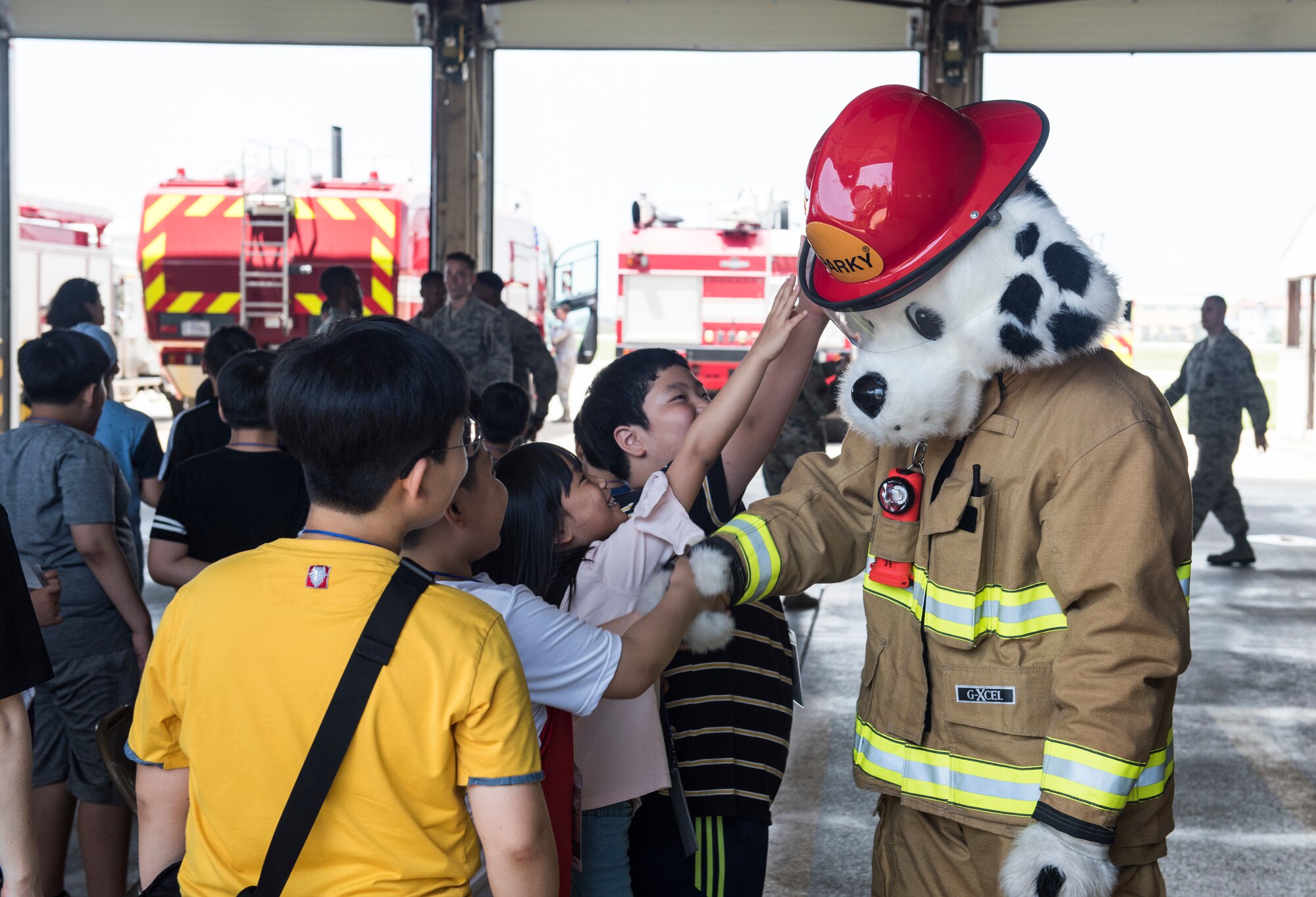 Korean children from the local area greet Sparky, the 8th Civil Engineer Squadron fire department mascot, during a tour at Kunsan Air Base, Republic of Korea, Aug. 2, 2019. Their visit included a chance to get hands-on with some firefighting equipment and see one of the fire trucks use its water cannon. (U.S. Air Force photo by Senior Airman Stefan Alvarez)