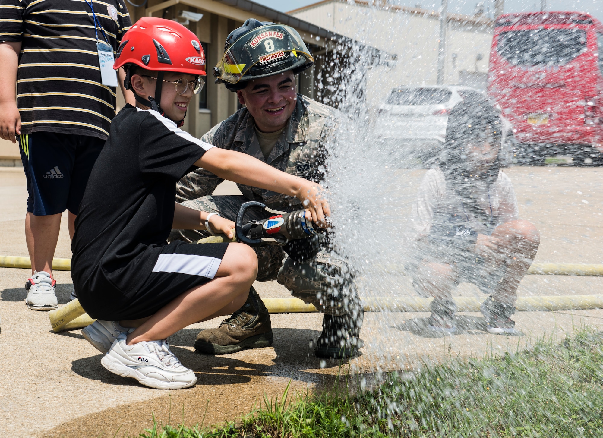 U.S. Air Force Senior Airman Jacob Levee, 8th Civil Engineer Squadron firefighter, helps a Korean child operate a fire hose during a tour at Kunsan Air Base, Republic of Korea, Aug. 2, 2019. Their visit included a chance to get hands-on with some firefighting equipment and see one of the fire trucks use its water cannon. (U.S. Air Force photo by Senior Airman Stefan Alvarez)