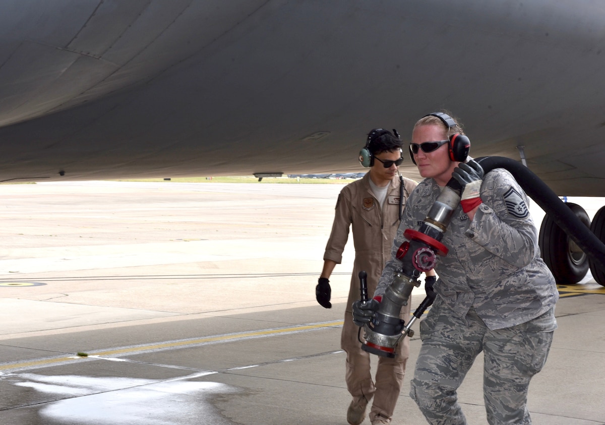 Airman pulls aircraft fuel hose over left shoulder and walks towards the front of aircraft.