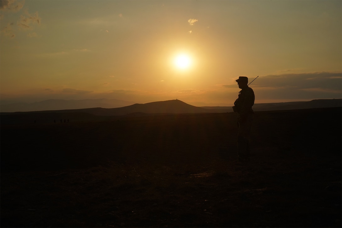 A soldier stands while the sun sets in the background.