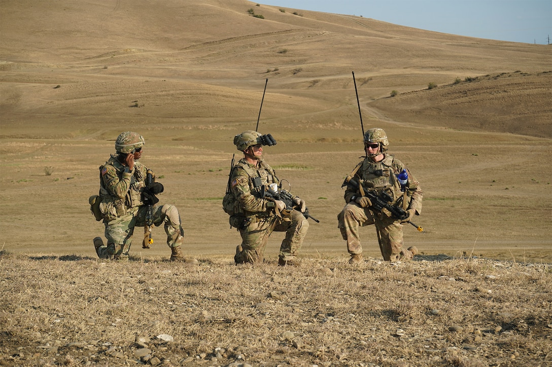 Three soldiers stand on a knee in a field.