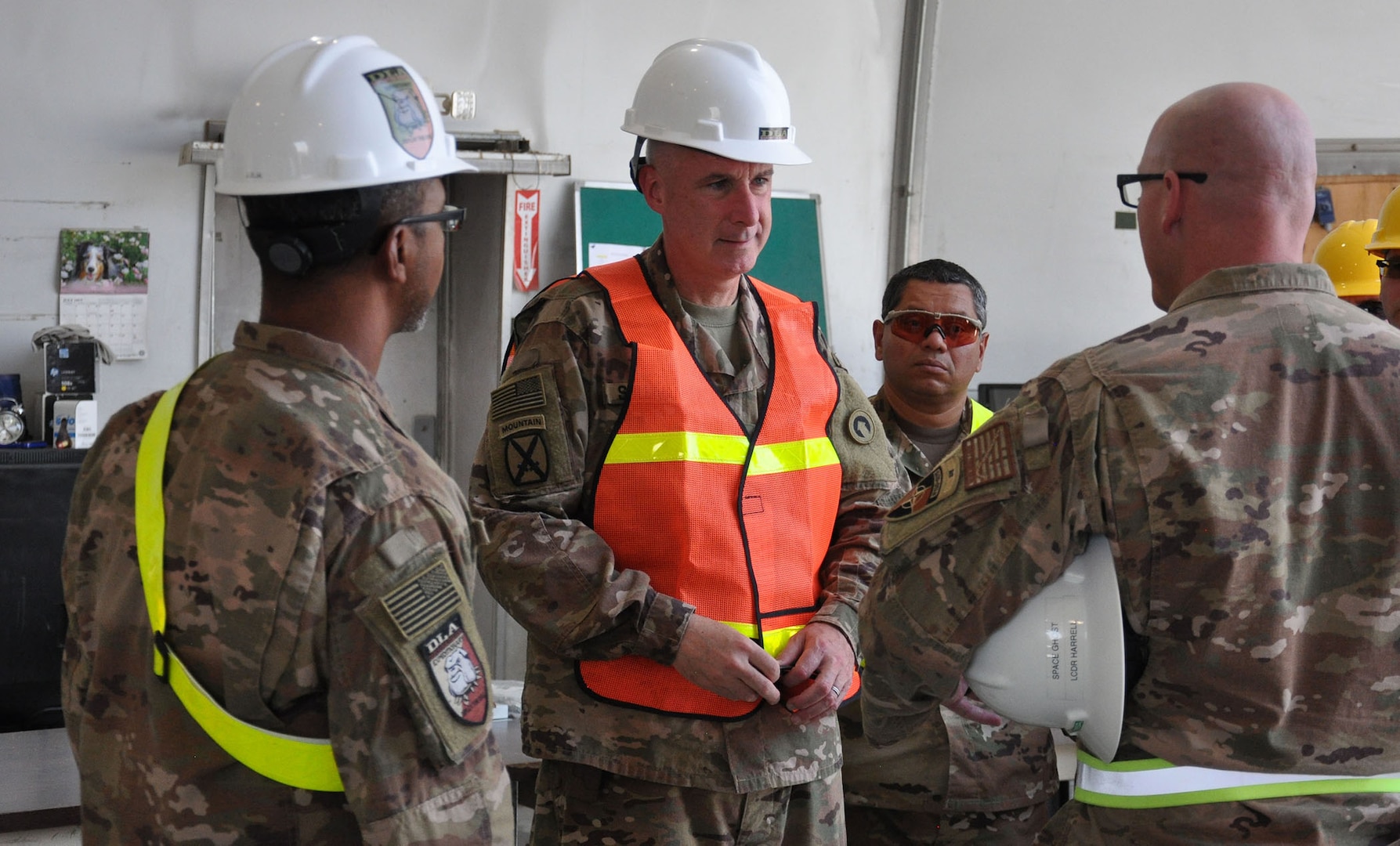 Army Maj. Gen. John Sullivan (center) listens as Navy Lt. Cmdr. Steve Harrell, officer in in charge of DLA Disposition Services-Afghanistan; briefs him before the tour in the receiving area of the Bagram DLA Disposition Services site.  Also shown are Jose Montanez (far left), Bagram site chief; and Navy Chief Petty Officer Michell Valencia (far right), Bagram deputy site chief.