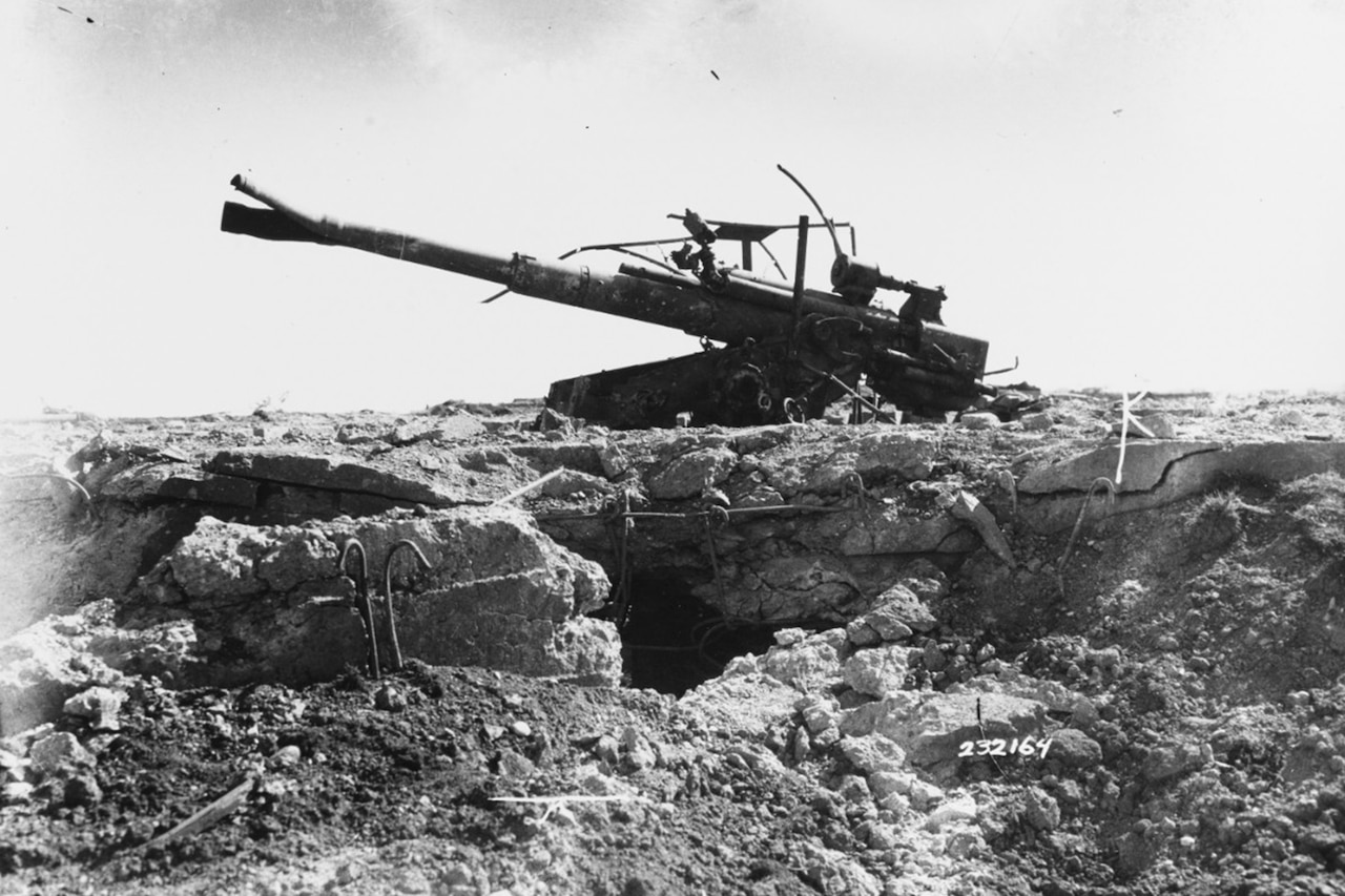 A German machine gun sits broken in a pile of rubble.