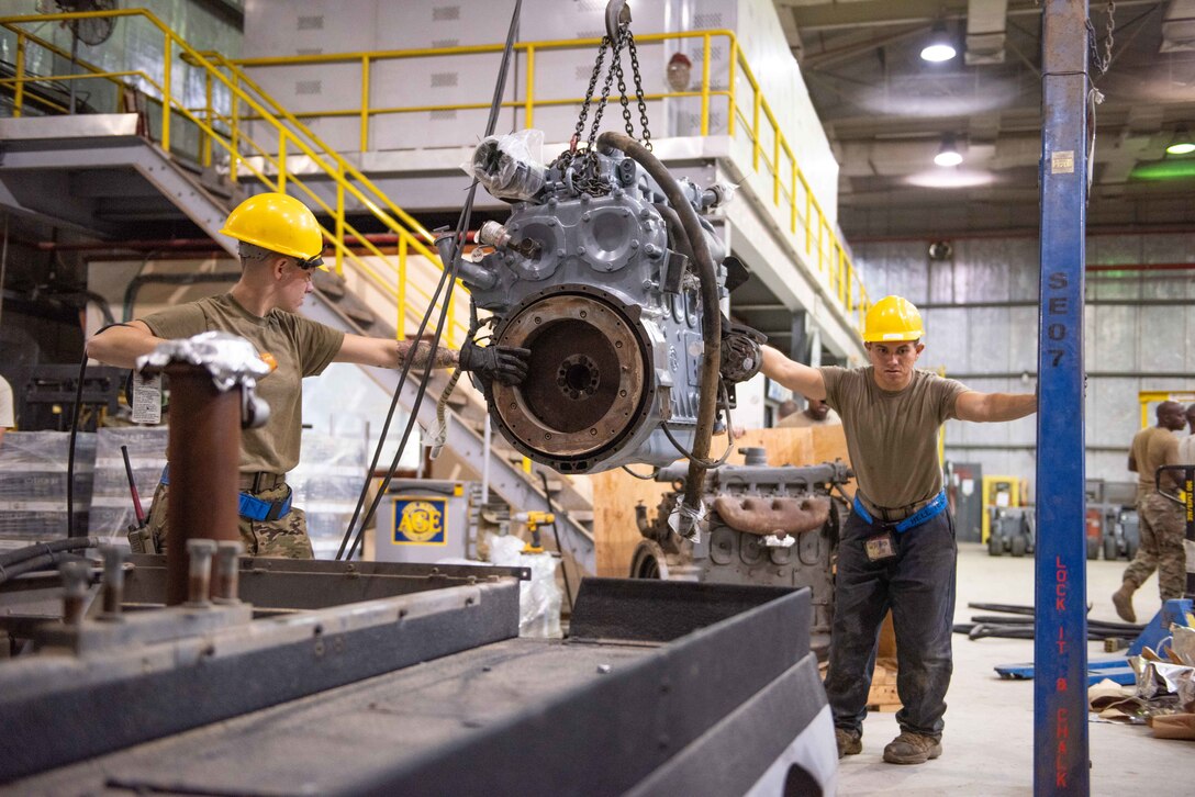 Staff Sgt. Adan Nunez and Senior Airman Maeson Bella, 380th Expeditionary Maintenance Squadron aerospace ground equipment technicians, lift a diesel engine to place into a -86 power cart July 30, 3019, at Al Dhafra Air Base, United Arab Emirates. Removing the old engine, rebuilding installing the new engine is a three-day process. (U.S. Air Force photo by Staff Sgt. Chris Thornbury)