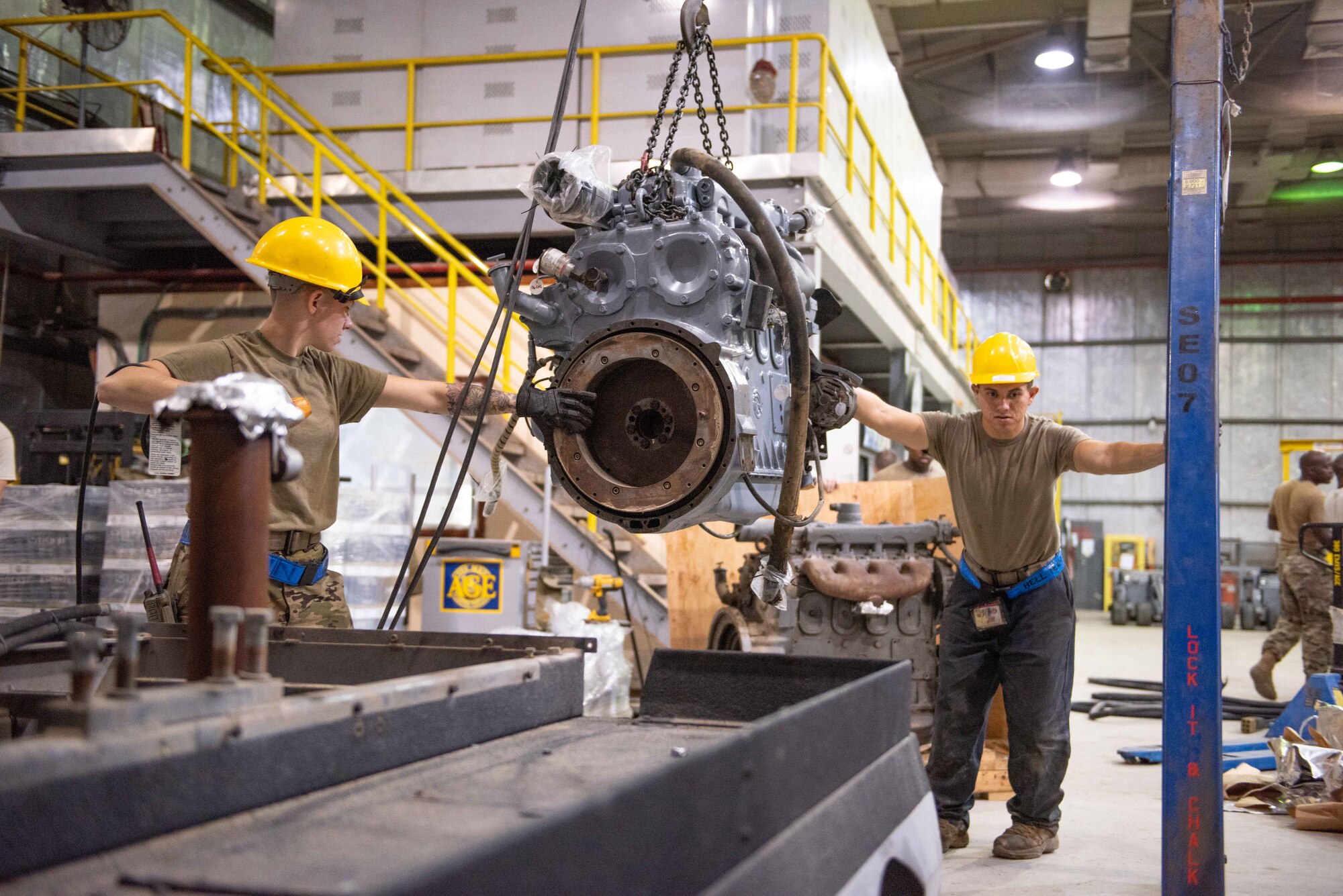 Staff Sgt. Adan Nunez and Senior Airman Maeson Bella, 380th Expeditionary Maintenance Squadron aerospace ground equipment technicians, lift a diesel engine to place into a -86 power cart July 30, 3019, at Al Dhafra Air Base, United Arab Emirates. Removing the old engine, rebuilding installing the new engine is a three-day process. (U.S. Air Force photo by Staff Sgt. Chris Thornbury)