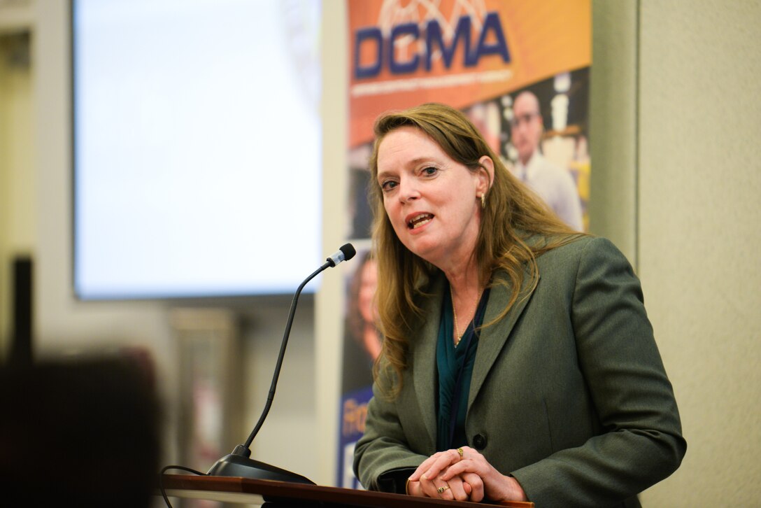 A woman speaks into a microphone from behind a stand.