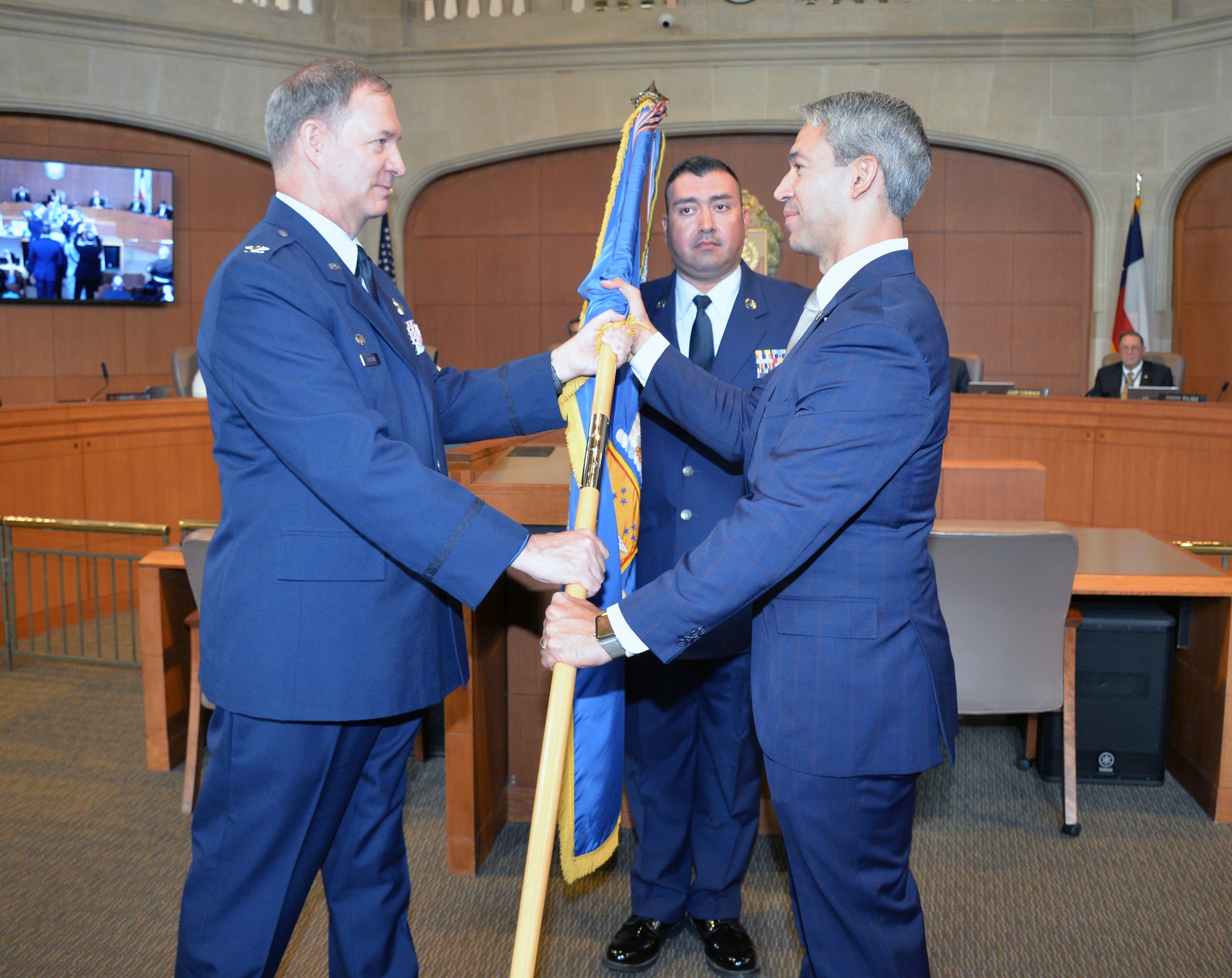 Col. Terry W. McClain, 433rd Airlift Wing commander, presents the wing guidon to San Antonio Mayor Ron Nirenberg during an honorary commander induction ceremony Aug. 8, 2019 in the city council chamber.