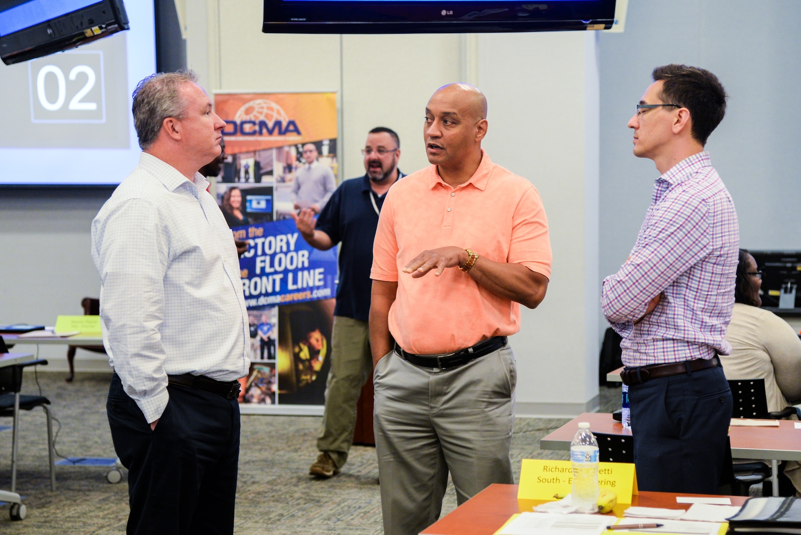 Three men stand in a room talking.