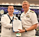 Rear Adm. Lorin Selby, Naval Sea Systems Command Deputy Commander for Ship Design, Integration and Engineering  presents Southwest Regional Maintenance Center  Sailor, Petty Officer 2nd Class Adam T. Barber, with a Letter of Commendation for his work advancing the scope of the Navy and Marine Corps Miniature/Micro-miniature Module Test and Repair Gold Disk Program during the Fleet Maintenance and Modernization Symposium at the San Diego Convention Center on August 8.