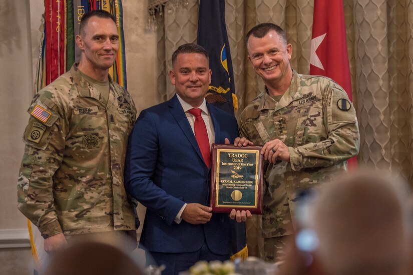 Gen. Paul E. Funk II, commanding general, U.S. Army Training and Doctrine Command, and TRADOC Command Sgt. Maj. Timothy A. Guden, pose for a photo with Ryan Klagenberg, the 2019 Reserve Instructor of the Year during the TRADOC Instructor of the Year Awards Ceremony, at Fort Eustis, Va., Aug. 7, 2019. The seven awardees were recognized at a ceremony during the TRADOC Commander's Forum.  (U.S. Army photo by Gwyndolynn Giacomo)