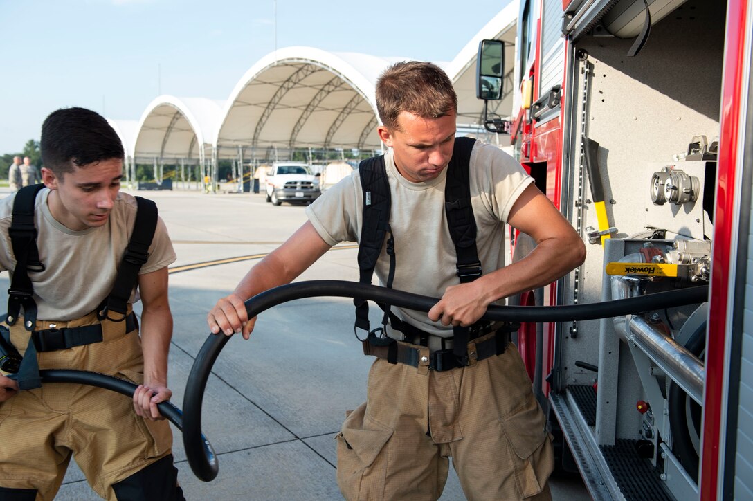 Senior Airman Tyler Goshe, left, and Airman 1st Class Zachary Mabee, both 23d Civil Engineer Squadron (CES) firefighters, wrap a hose after completing an A-10C Thunderbolt II egress training scenario, Aug. 9, 2019, at Moody Air Force Base, Ga The 23d CES conducted the exercise to test their capability in extinguishing an A-10 on fire while simultaneously rescuing its pilot. The training also served as an opportunity for firefighter crew chiefs and their Airmen to increase team cohesion. (U.S. Air Force photo by Airman Azaria E. Foster)
