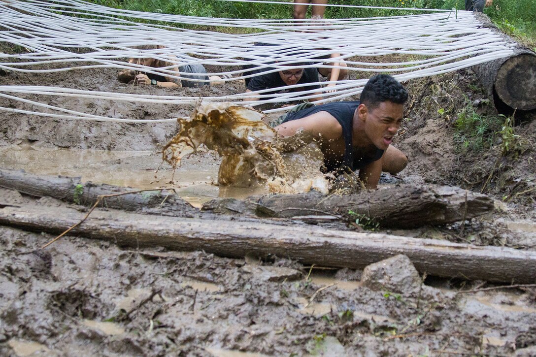 Soldiers and civilians climb under an obstacle.