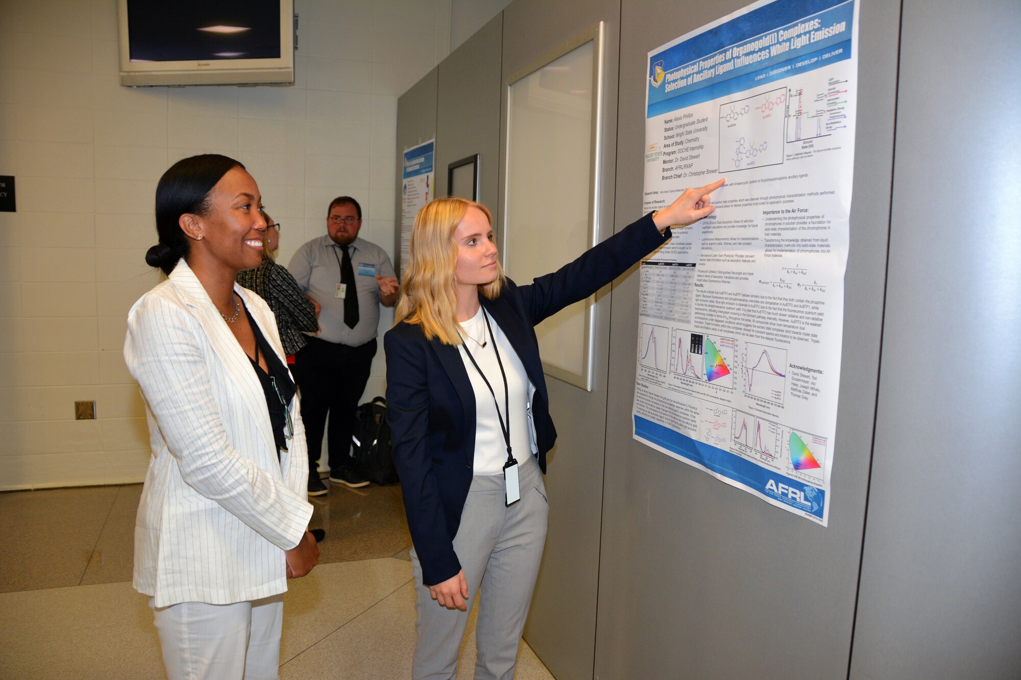 Alexis Phillips, an undergraduate student at Wright State University, presents her poster on Photophysical Properties of Organogold(I) Complexes: Selection of Ancillary Ligand Influences White Light Emission, to Asheley Blackford, who is in her fourth year of managing the student researcher poster session for AFRL’s Materials and Manufacturing Directorate. (U.S. Air Force photo/Spencer Deer)