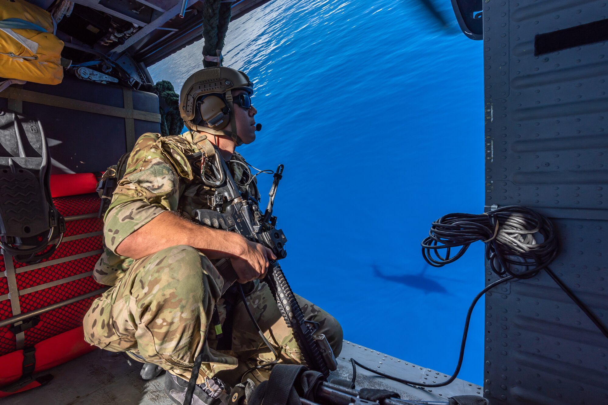 A U.S. Air Force pararescueman assigned to the 31st Rescue Squadron, looks out over the ocean while aboard an HH-60G Pave Hawk, July 26, 2019, out of Kadena Air Base, Japan. The 31st RQS consists of combat rescue officers, pararescue specialists and survival, evasion, resistance and escape specialists who work together to facilitate the return of isolated personnel back to friendly forces. (U.S. Air Force photo by Airman 1st Class Matthew Seefeldt)