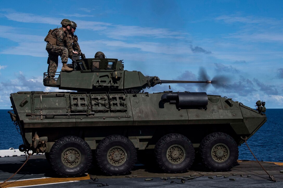 Marines fire a chain gun from the deck of a military ship.