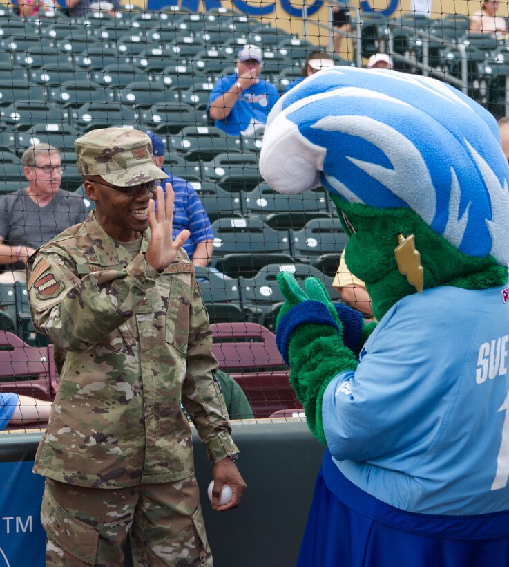 An Airman waves to a mascot at a baseball game.