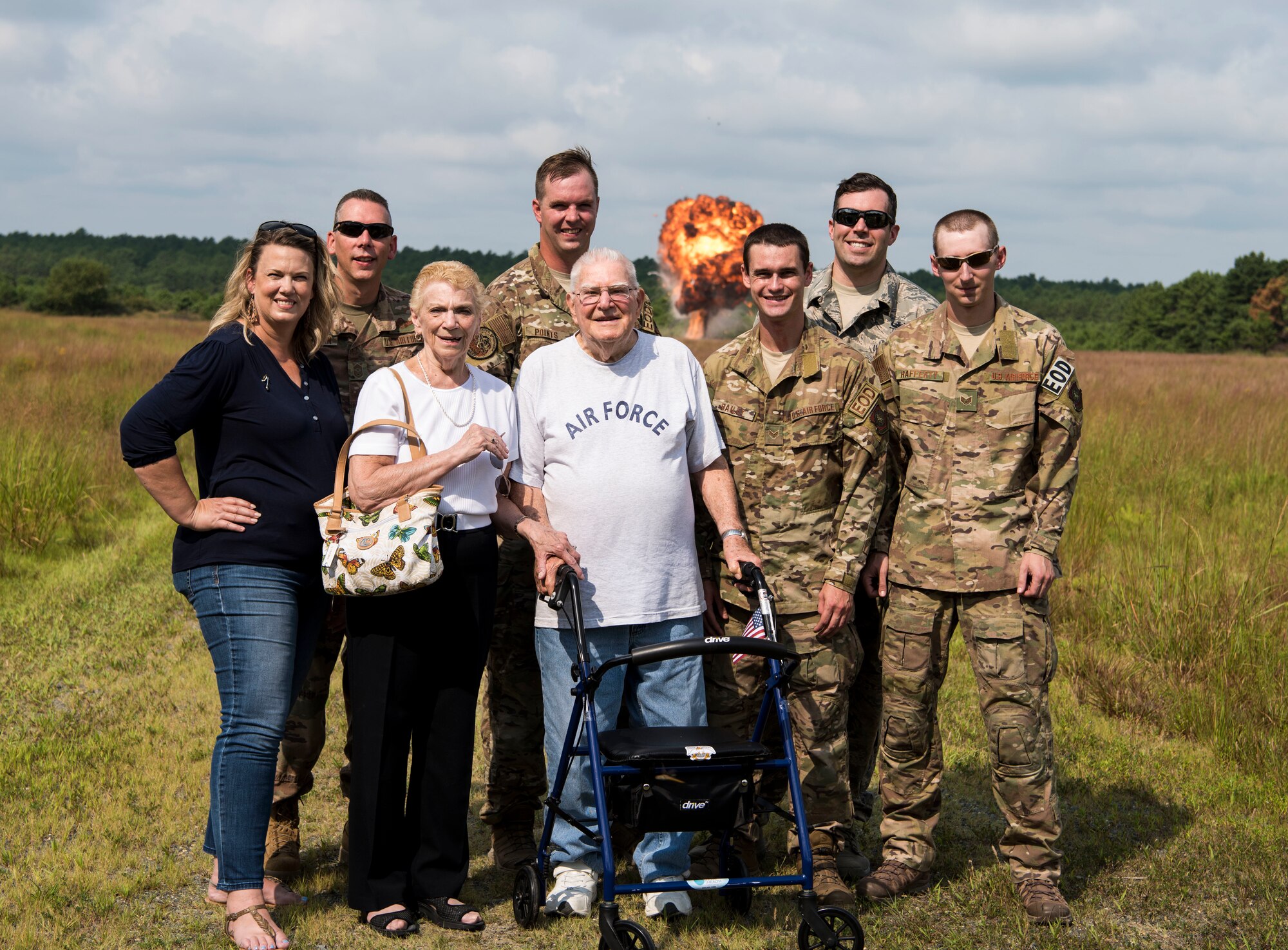 Joint Base McGuire-Dix-Lakehurst community members pose in front of a controlled explosion on Joint Base MDL, New Jersey, Aug. 7, 2019. The 87th Civil Engineer Squadron Explosive Ordnance Disposal team provided a tour of the unit and conducted a controlled detonation on the EOD proficiency range to John “Jack” McCarthy, retired U.S. Air Force Explosive Ordnance Disposal technician, (middle). (U.S. Air Force photo by Airman 1st Class Ariel Owings)