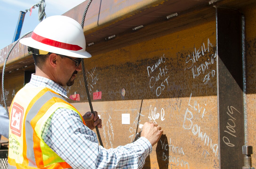 ALBUQUERQUE, N.M. - Filemon Gallegos, project manager, USACE Albuquerque District for the National Nuclear Security Administration Albuquerque Complex, signs the beam prior to being placed. The event celebrated the emplacement of the last steel beam, a milestone in completing the structure. Coins from NNSA, SPA and Caddell Construction were glued to the beam. Lt. Col. Caswell, commander, Albuquerque District; Lisa Gordon-Haggerty, administrator, NNSA; Jeff Caddell, contractor for the project, and many other participants also had the opportunity to sign the beam.