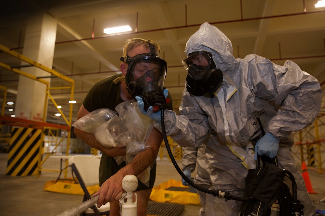 U.S. Marine Corps Lance Cpl. Mary Lou Cummings, right, prepares to remove the self-contained breathing apparatus from Lance Cpl. Phoenix Drohan as he exits the decontamination area during a training exercise at Camp Kinser, Okinawa, Japan, August 1, 2019.  Once the apparatus is removed, Marines must hold their breath and keep their eyes closed until they are safely away from the decontamination area. Cummings, a native of Boston, Massachusetts, and Drohan, a native of San Diego, California, are both CBRN defense specialists with G-3, Enhanced CBRN Section, Combat Logistics Regiment 37, 3rd Marine Logistics Group. (U.S. Marine Corps photo by Lance Cpl. Carla E. O)