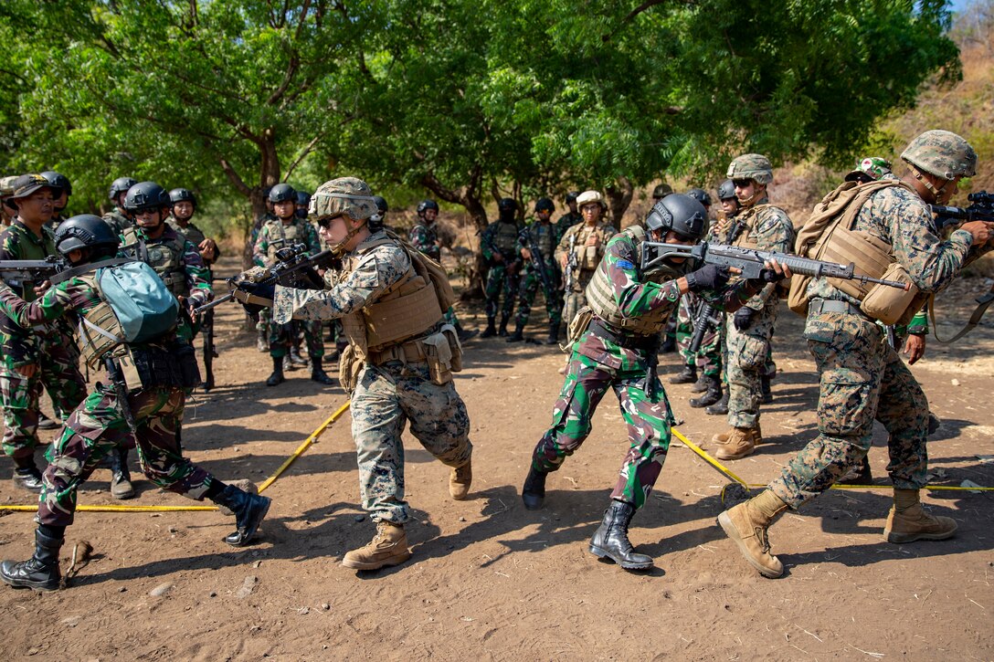 Marines holding guns run in different directions.