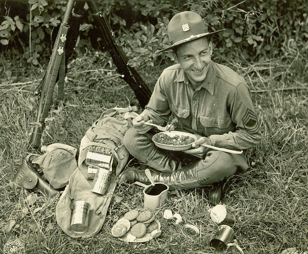 A soldier sits on the ground eating C-rations.