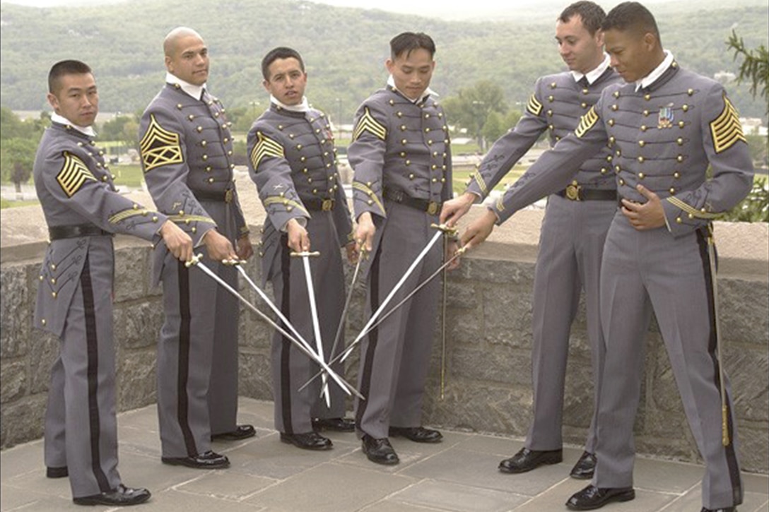 Army cadets pose in a half circle with their swords drawn in their graduation uniforms.