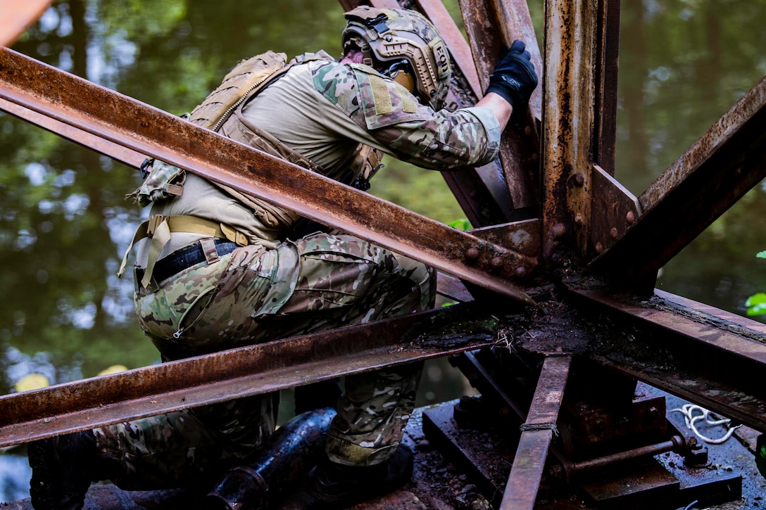 A sailor checks a fake explosive device on a metal beam.