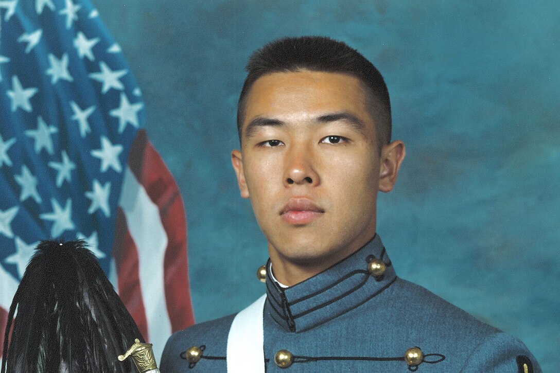 Army cadet holding his cap and sword in a portrait in his graduation uniform.