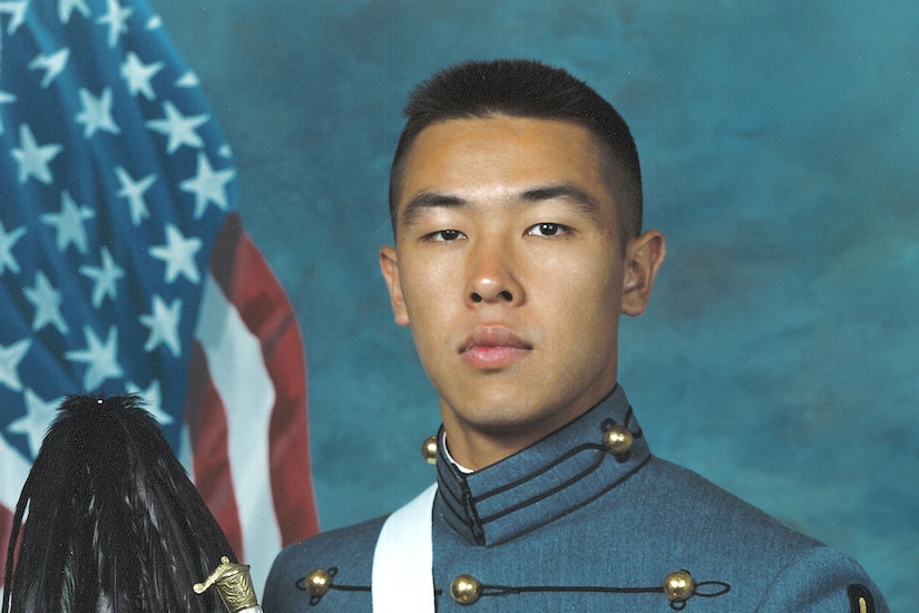 Army cadet holding his cap and sword in a portrait in his graduation uniform.