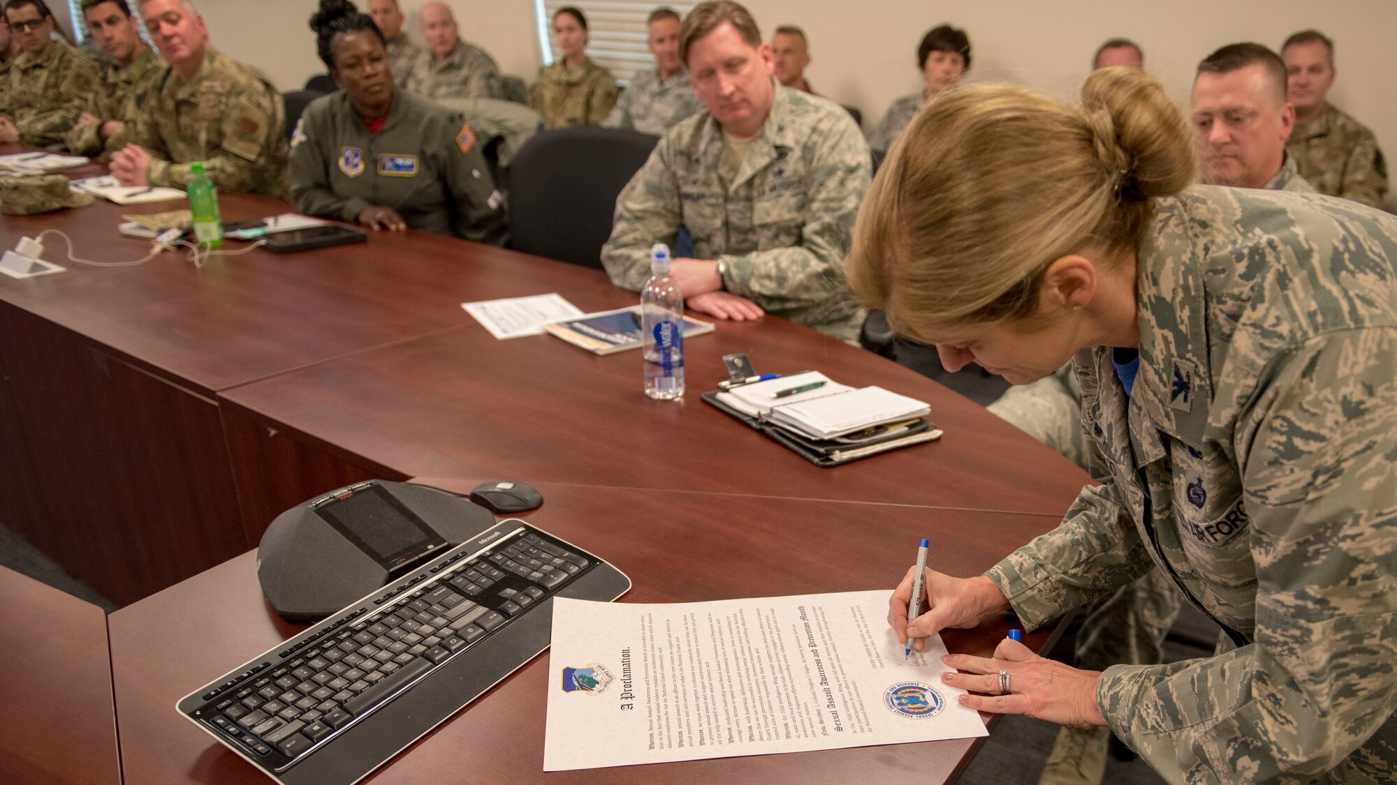 102nd Intelligence Wing commander Col. Virginia I. Gaglio signs declaration as Airmen look on.