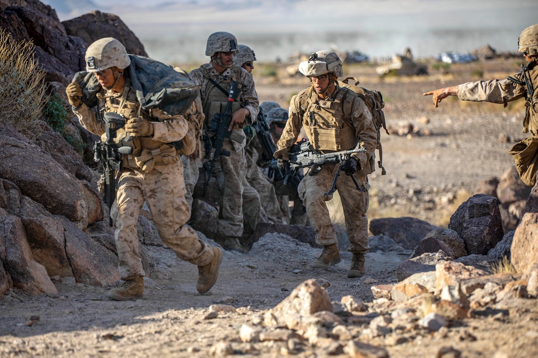 Marines walk with weapons on desert-type terrain.