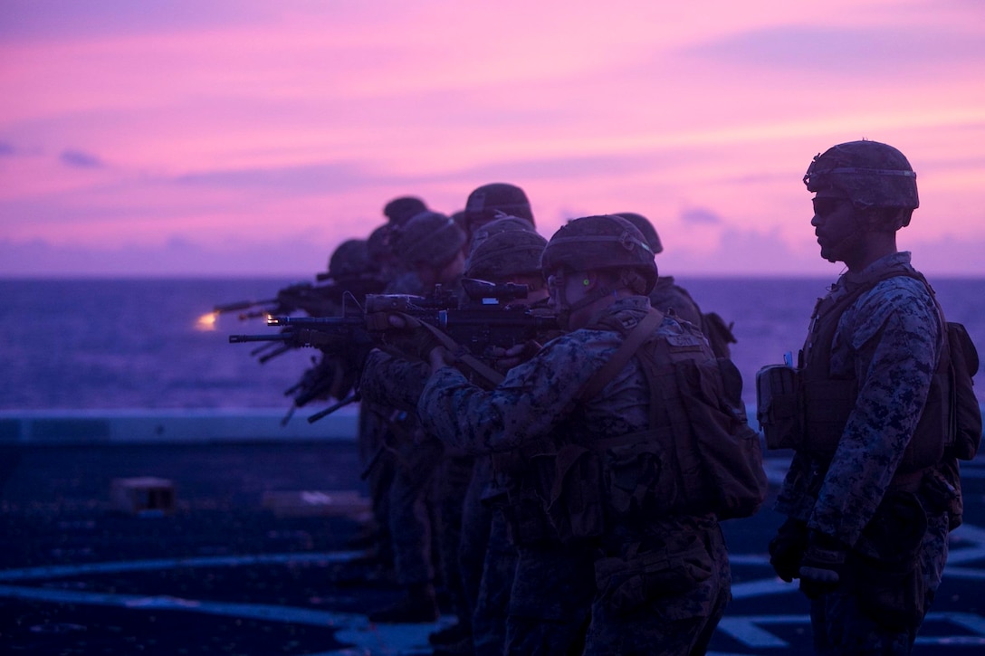 Marines stand in a line shooting from rifles.