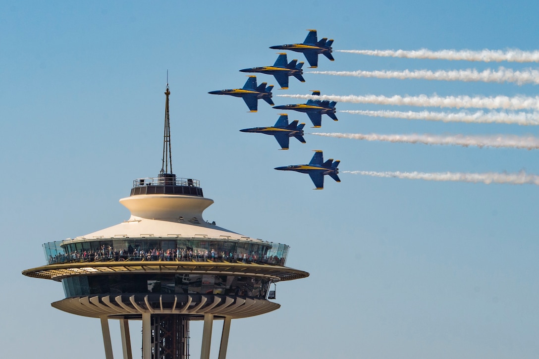 Military aircraft fly by the top of a building.