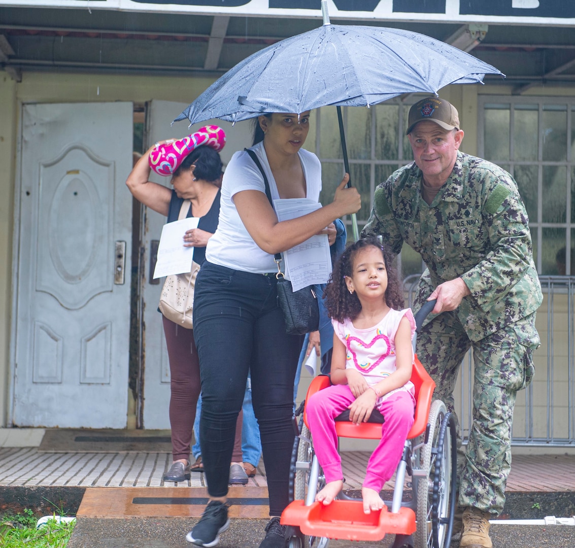 A military member pushes a child in a wheelchair.