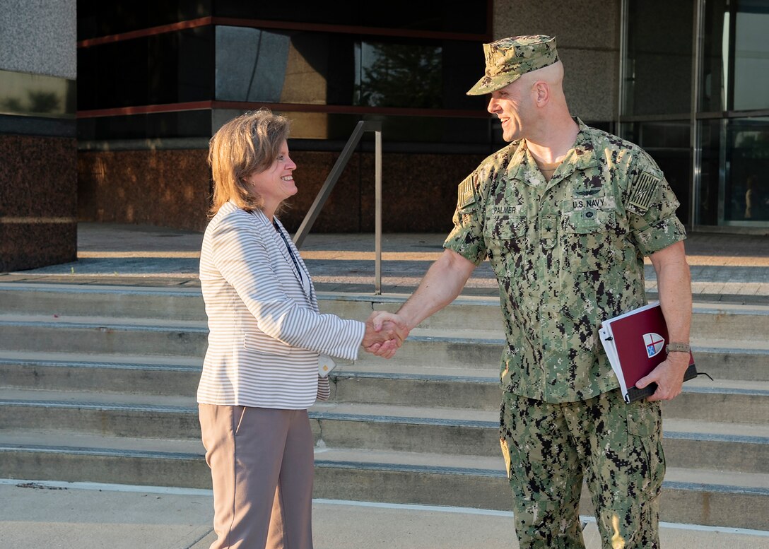 Navy Admiral greets Defense Logistics Agency Chief of Staff  in front of Land and Maritime Headquarters building.