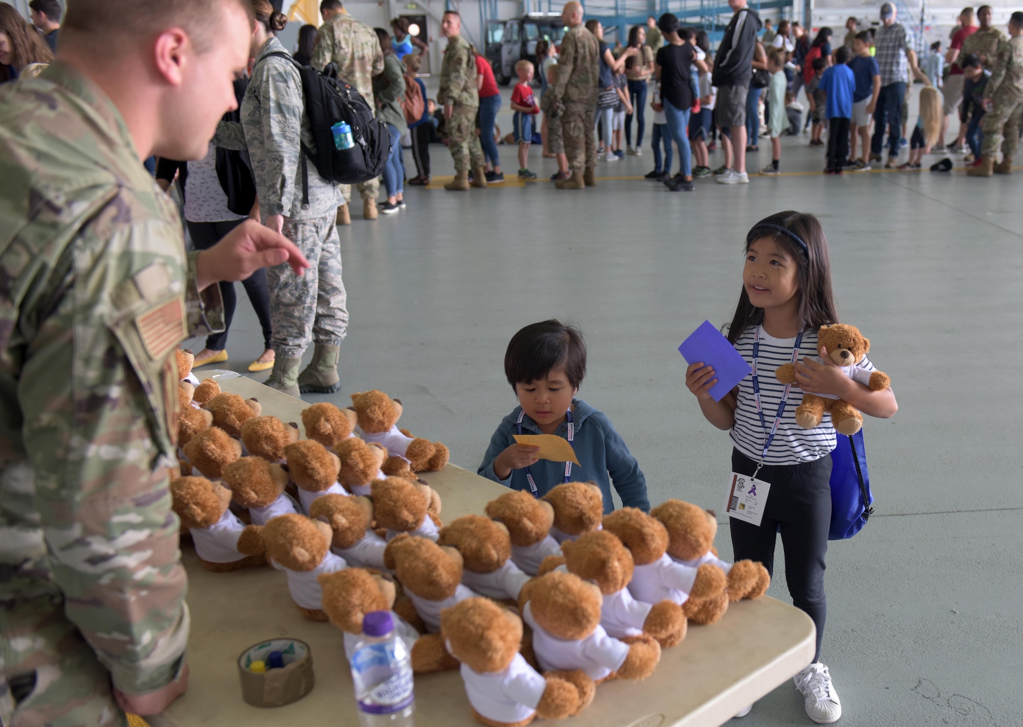 A child receives a teddy bear and a stamp for her paper while in-processing during the ‘kids deployment line’ at RAF Mildenhall, England, Aug. 9, 2019. The third annual Operation Together and Ready, helped the families of Team Mildenhall  learn what Airman go through to prepare for a deployment. (U.S. Air Force photo by Senior Airman Benjamin Cooper)