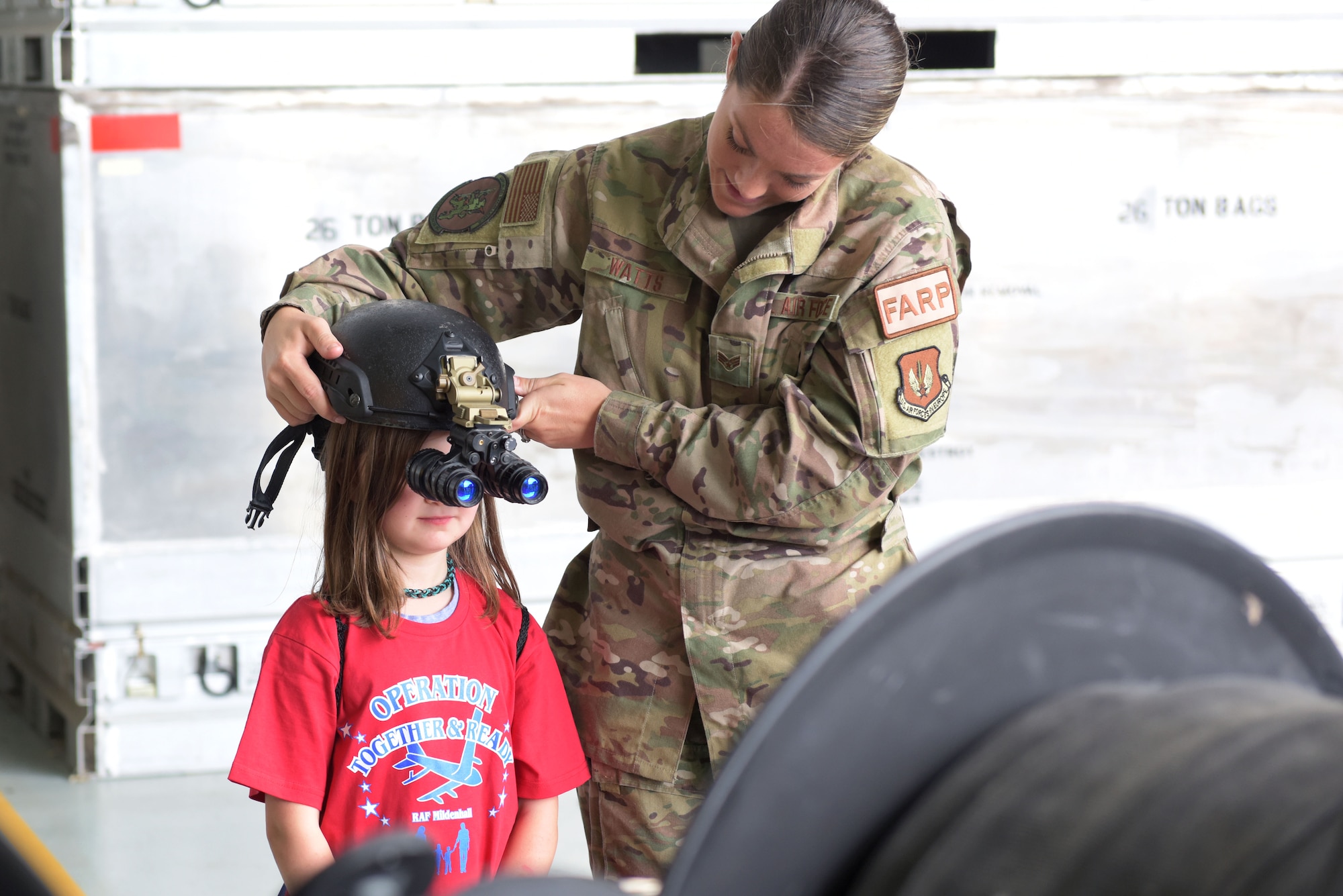 Senior Airman Tori Watts, 100th Logistics Readiness Squadron fuels distribution operator, helps a child try on night-vision goggles during the ‘kids deployment line’ at RAF Mildenhall, England, Aug. 9, 2019. The children were able to understand how Forward Arming and Refuling Point Airmen perform their job at night. (U.S. Air Force photo by Senior Airman Benjamin Cooper)