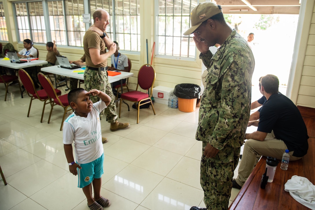 A child salutes a military person.