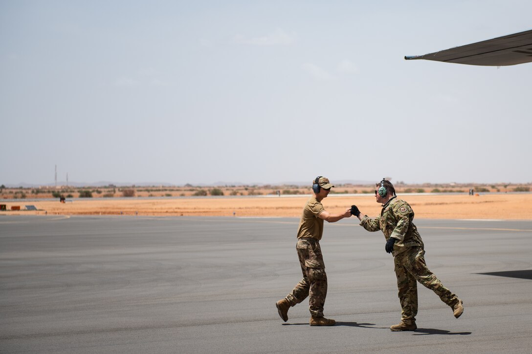 U.S. Air Force Staff Sgt. Dustin Cote, 724th Expeditionary Air Base Squadron air terminal operations center technician, left, bumps fists with Staff Sgt. John Bouscher, 86th Aircraft Maintenance Squadron flying crew chief, after the first C-130 landing at Nigerien Air Base 201, Agadez, Niger, Aug. 3, 2019. The landing marked the next step in airfield evaluations by starting Visual Flight Rules operations at the base. (U.S. Air Force photo by Staff Sgt. Devin Boyer)