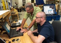 Photo of Robert Judd teaching Will Fobes how to confirm Army Close Access Target Reconnaissance (CATR) kits are fully mission capable prior to use in the field.