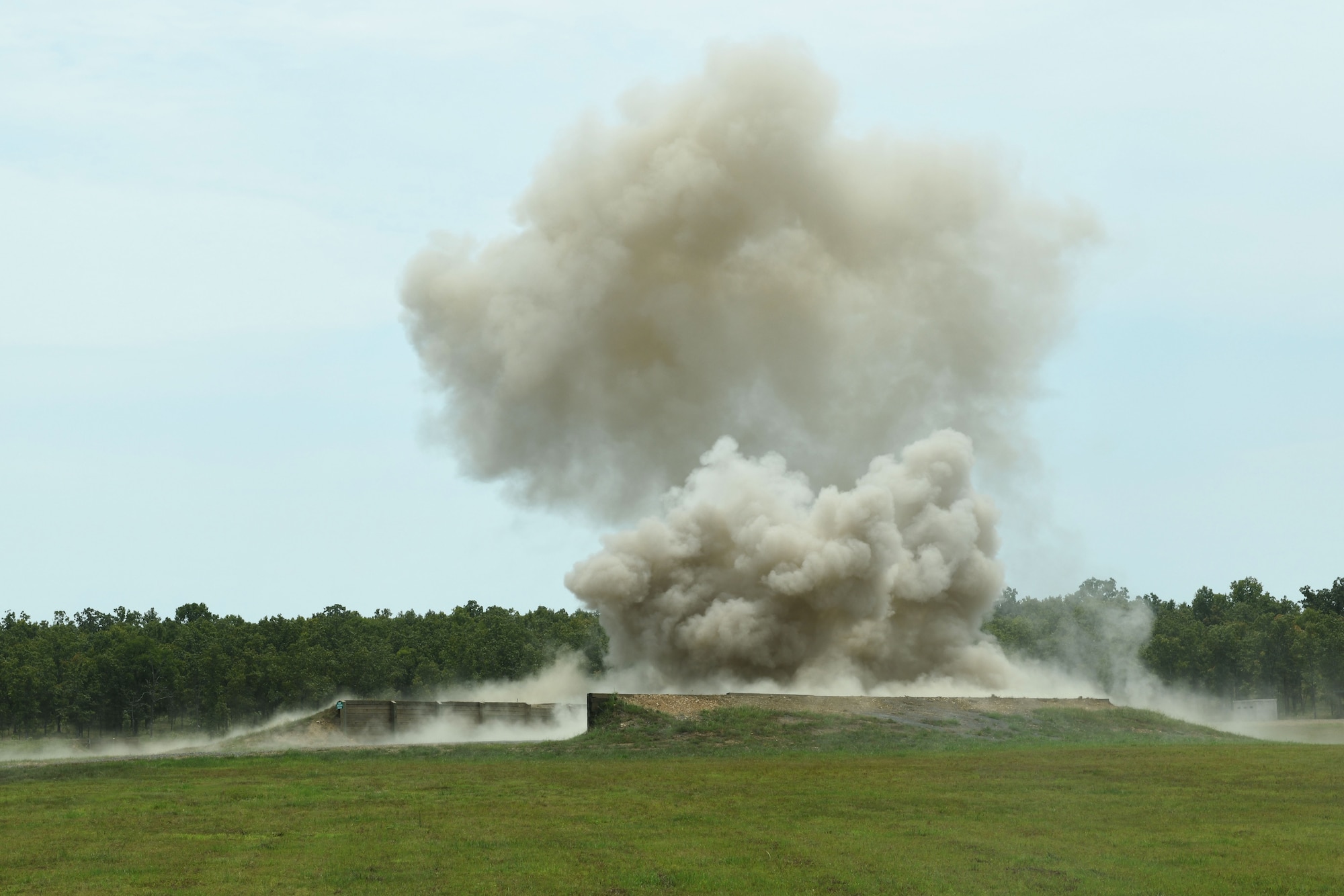 A cloud of smoke and dirt flies off a green grassy field.