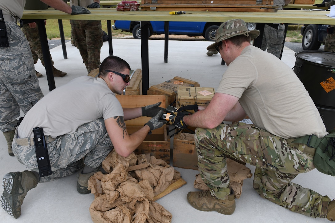 Two men kneel over small wodden boxes while one holds a smaller brown box.