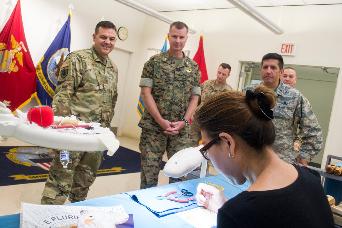 Air Force Col. Gabriel Lopez, DLA Aviation Ogden commander, left, Marine Corps Col. Larry Herring, center, and Air Force Col. John Gustafson, right, the DLA Aviation Richmond Marine Corps and Air Force Customer Facing Division chiefs, respectively, watch Helen Nguyen, DLA Troop Support Flag Room seamstress, as she hand embroiders a presidential flag Aug. 14, 2019 in Philadelphia.