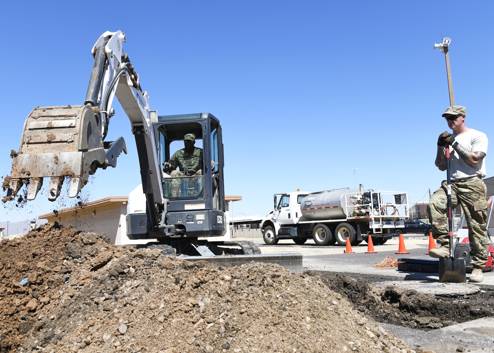 Tech. Sgt. Ronnie Jamison, 56th Civil Engineering Squadron pavements and heavy equipment operator uses a mini excavator to dig in the road while Staff Sgt. Robert Newton, 56th CES pavements and heavy equipment operator, ensures the mini excavator doesn’t cause damage during a valve replacement project Aug. 12, 2019, at Luke Air Force Base, Ariz.