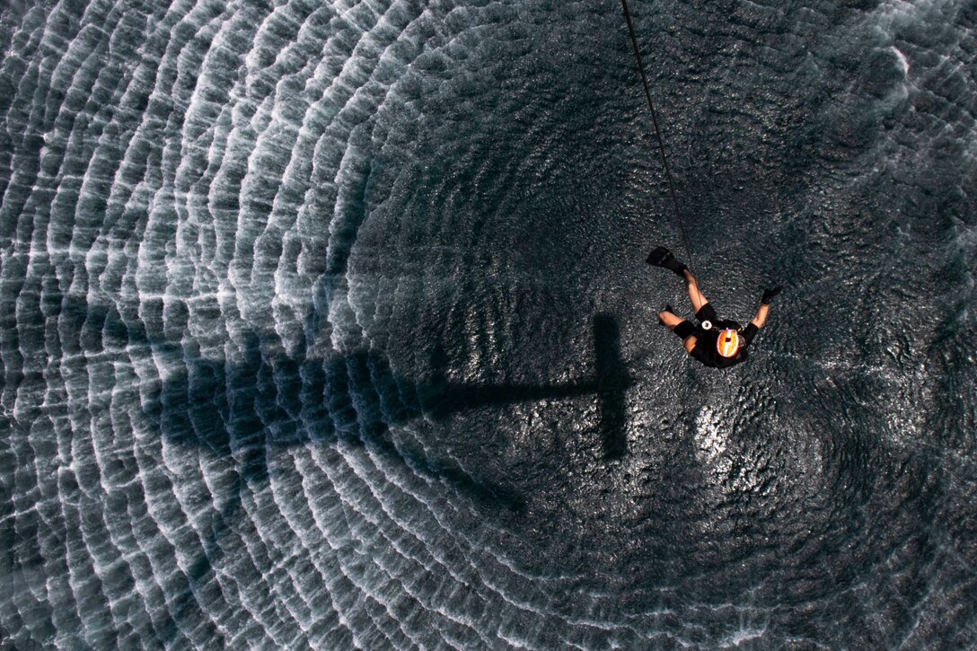 A sailor rappels from a rope above water.