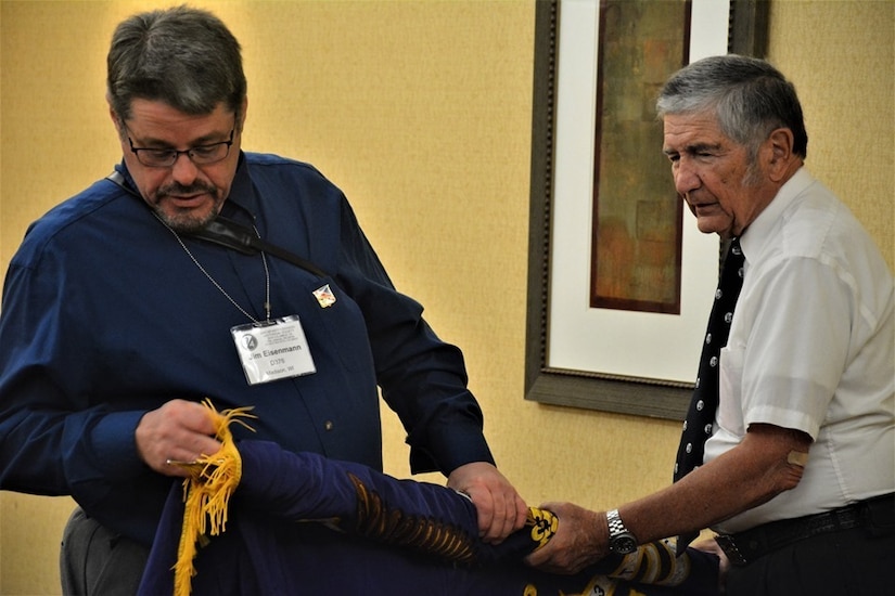 John Clyburn (right), secretary of the 94th Infantry Division Historical Society, holds the 94th's colors as Jim Eisenmann carefully furls and cases them at the society's reunion banquet.  World War II veterans, their families, and current members of the 94th Training Division-Force Sustainment came together to celebrate the 70th anniversary of the 94th IDHS at their annual reunion held in Columbus, Georgia, June 14-15, 2019.